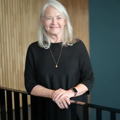 dame som står ved rekkverk inne på et kontor smiler