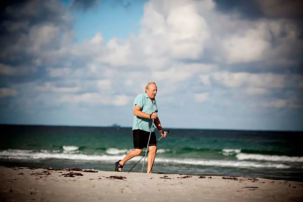 Mann går med staver, på ei Jærstrand. Foto.