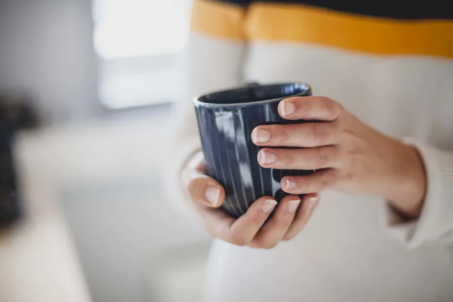 Person som holder en kaffekopp i hånda. Foto.