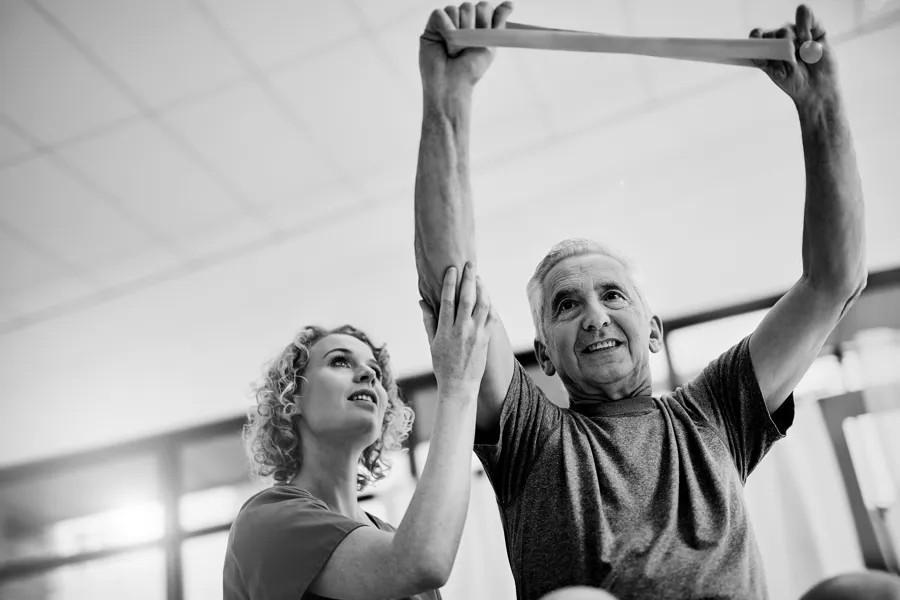 Svart hvitt foto sykepleier hjelper eldre mann med trening